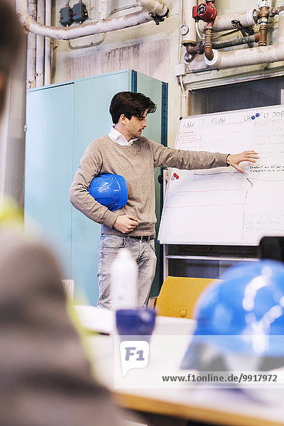 Junger männlicher Arbeiter bespricht Plan auf Whiteboard mit Kollegen in der Fabrik