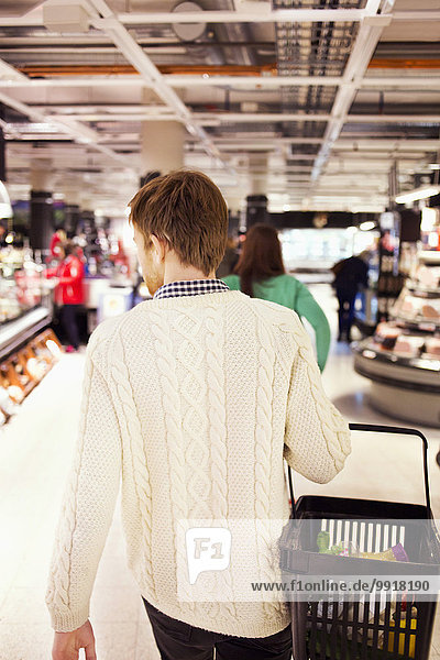 Rückansicht des Mannes mit Korb beim Spaziergang im Supermarkt
