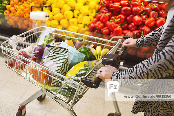 Mittelteil der Frau beim Einkaufen im Einkaufswagen im Supermarkt