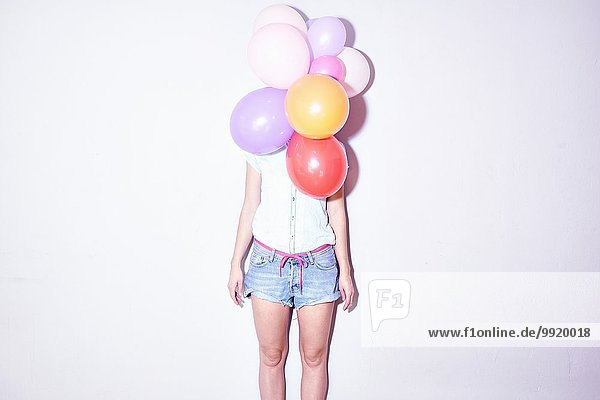 Studioaufnahme einer jungen Frau  die hinter einem Haufen Luftballons steht.