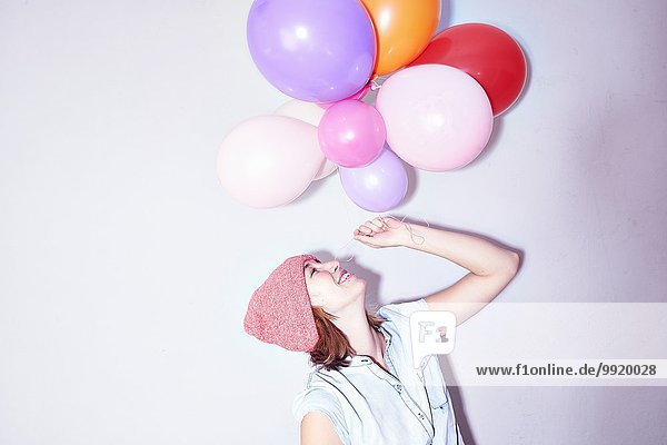 Studioaufnahme einer jungen Frau  die einen Haufen Luftballons hochhält.