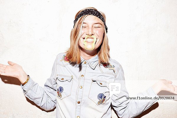 Studioaufnahme einer jungen Frau mit gelber Kaugummiblase im Mund