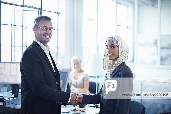 Porträt einer jungen Geschäftsfrau beim Händeschütteln mit Geschäftsmann im Amt