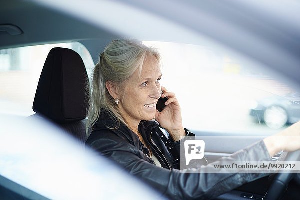 Reife Geschäftsfrau chattet auf dem Smartphone beim Autofahren