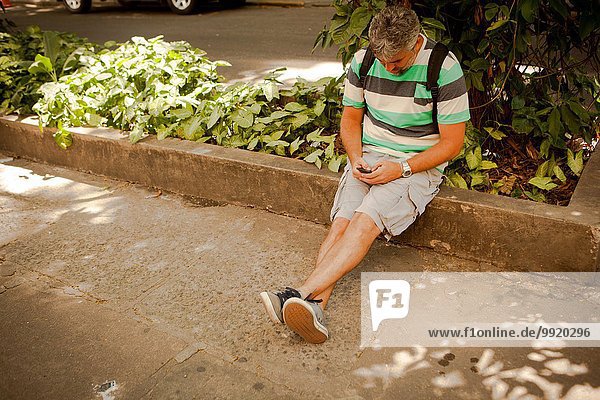 Erwachsener Mann auf dem Bürgersteig sitzend  SMS auf dem Smartphone  Rio De Janeiro  Brasilien