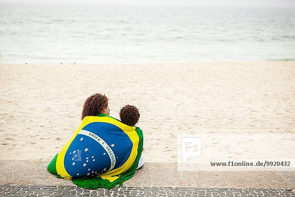 Rückansicht von Mutter und Sohn in brasilianischer Flagge am Strand von Ipanema Rio De Janeiro Brasilien