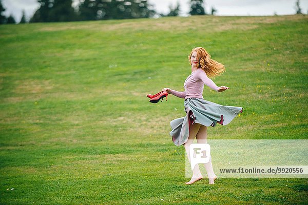 Portrait of young woman dancing in park holding red high heels