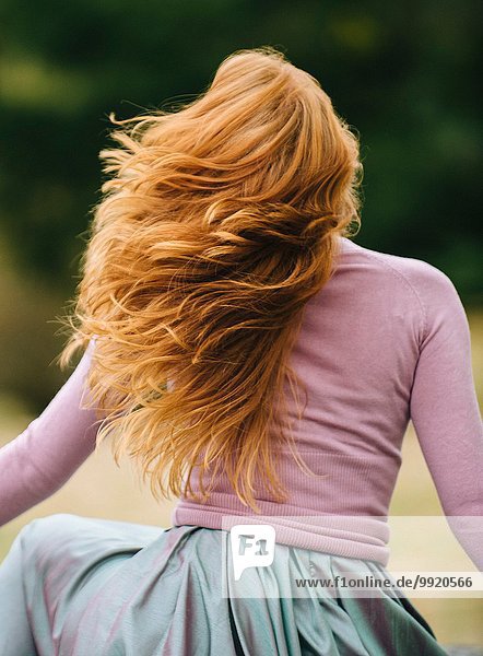 Rear view of young woman with long red hair twirling in park