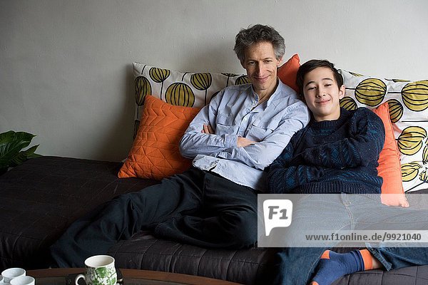 Portrait of father and teenage son relaxing on sofa