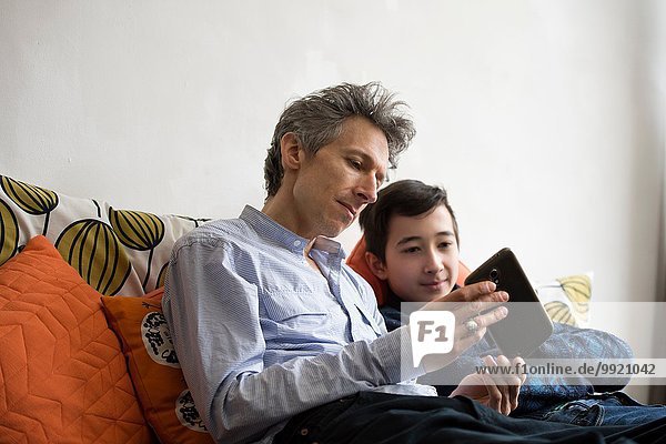 Teenage boy and father reading smartphone texts on sofa