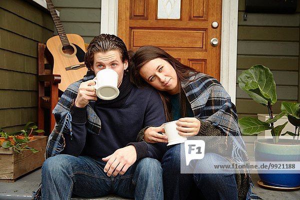 Junges Paar auf der Veranda  eingehüllt in eine Decke  die Kaffee trinkt.