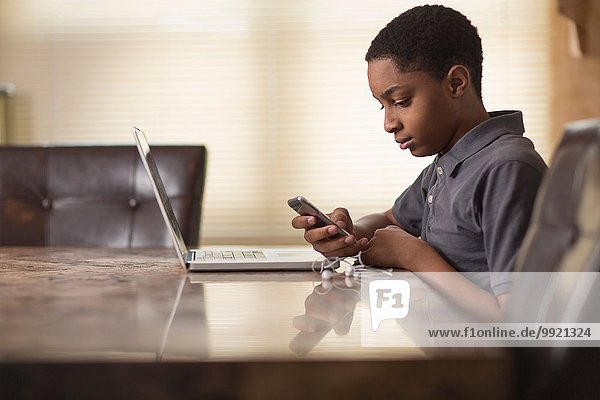 Teenager-Junge am Esstisch beim Lesen von Smartphone-Texten