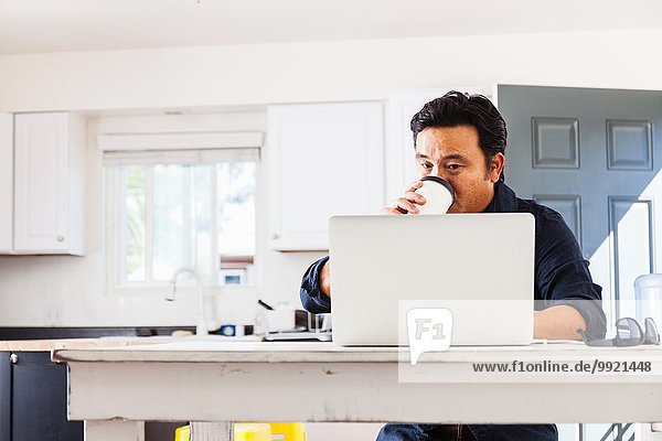 Reife Geschäftsleute  die auf dem Laptop tippen und Kaffee zum Mitnehmen am Küchentisch trinken.