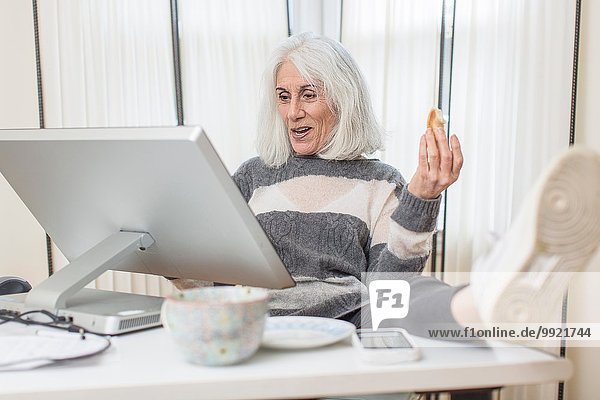 Porträt einer älteren Frau am Computer sitzend mit Fuß auf dem Schreibtisch