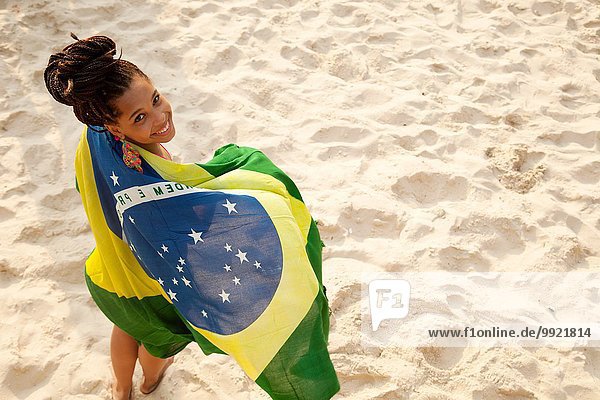 Overhead portrait of young woman wrapped in Brazilian flag  Ipanema beach  Rio De Janeiro  Brazil