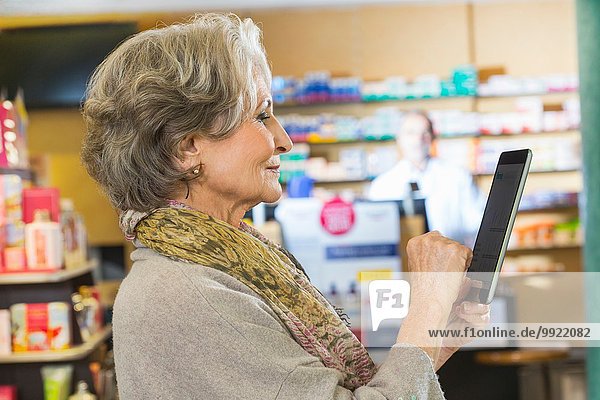 Senior woman using digital tablet to check medicine online in pharmacy