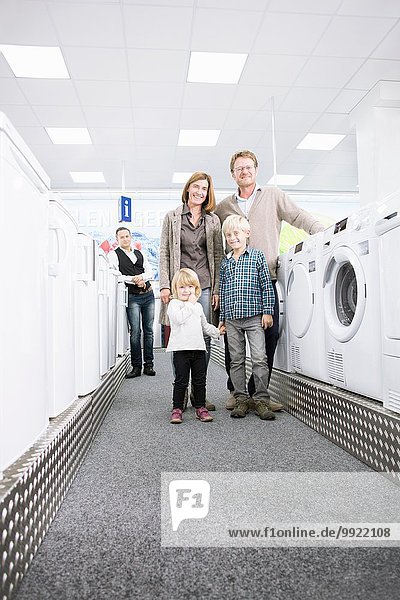 Porträt einer Familie mit zwei Kindern beim Durchstöbern von Waschmaschinen im Elektronikgeschäft