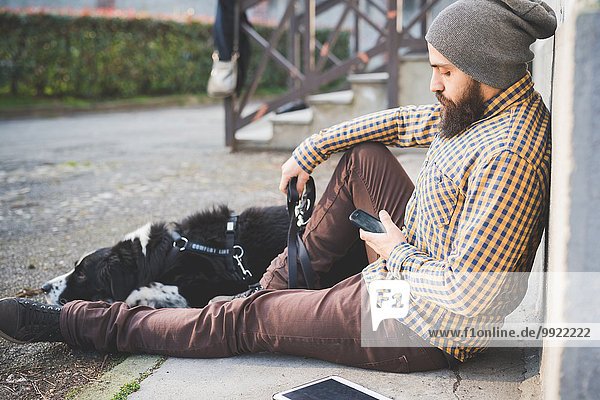 Mittlerer Erwachsener Mann  der mit Hund im Freien sitzt  mit Smartphone