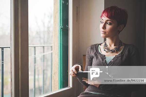 Junge Frau am Fenster sitzend  mit digitalem Tablett