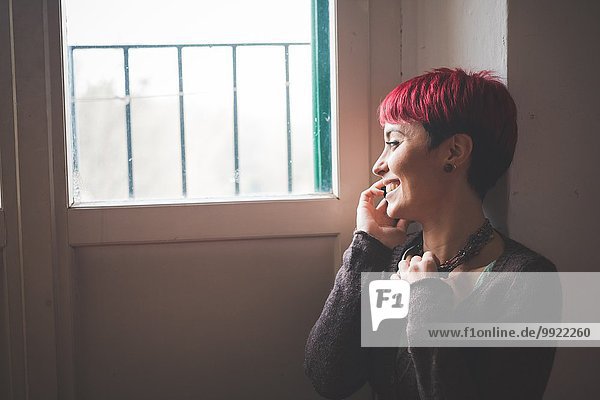 Junge Frau am Fenster sitzend  am Handy sprechend