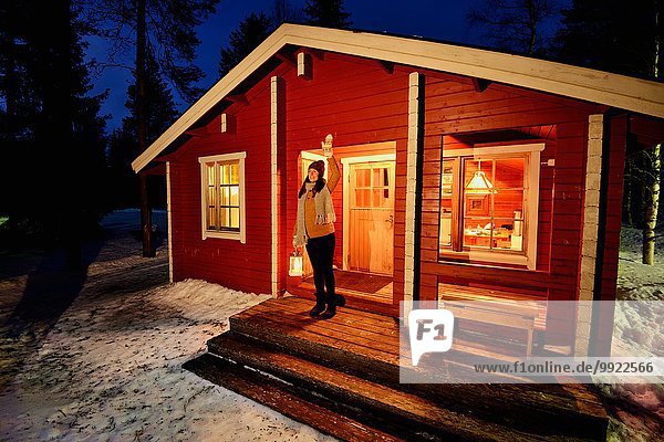 Young woman looking out from cabin porch at night  Posio  Lapland  Finland