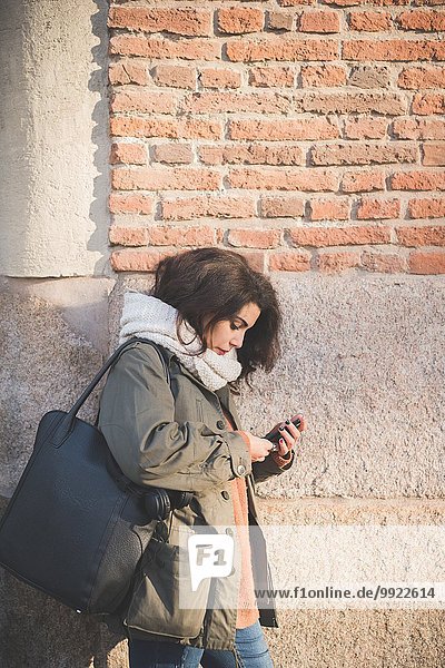 Junge Frau  die sich an die Wand lehnt und Smartphone-Texte liest.