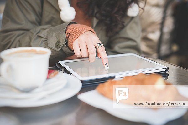 Ausschnittaufnahme einer jungen Frau mit Touchscreen auf einem digitalen Tablett im Straßencafé