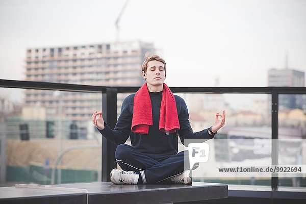 Young man practicing lotus yoga position on city rooftop