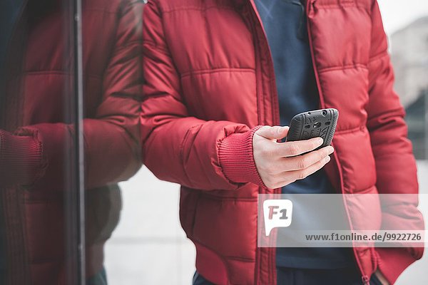 Schnappschuss eines jungen Mannes  der sich gegen ein Bürogebäude lehnt und Smartphone-Texte liest.
