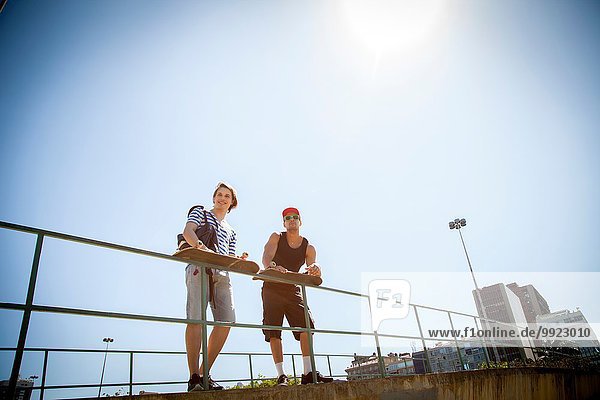 Two men  holding skateboards  leaning on railings  low angle view