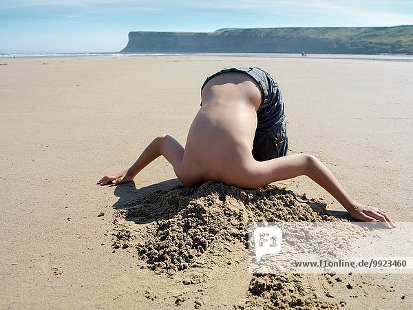Junge mit Kopf im Sand am Strand vergraben