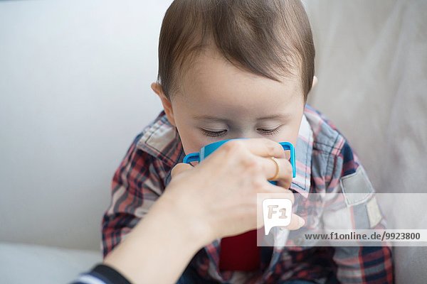 Mother helping baby boy drink from cup