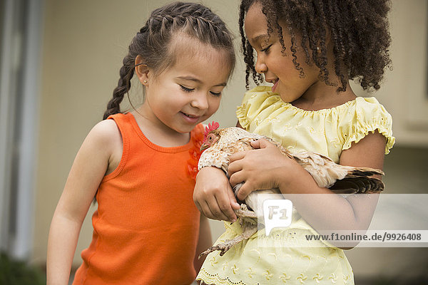 Two young girls  one holding a chicken in her arms.