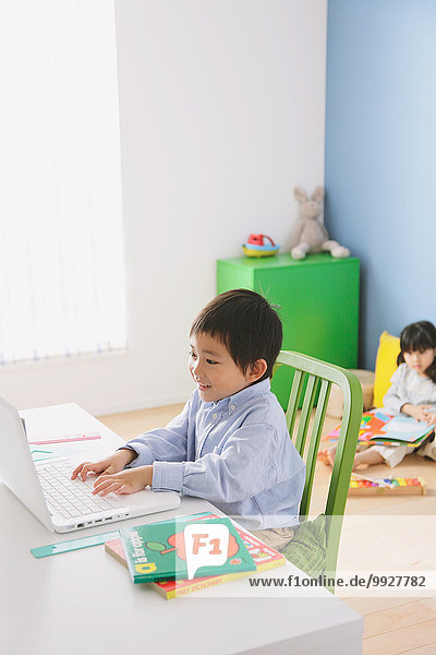 Elementary age boy doing his homework at his desk with his sister reading on the floor in the background