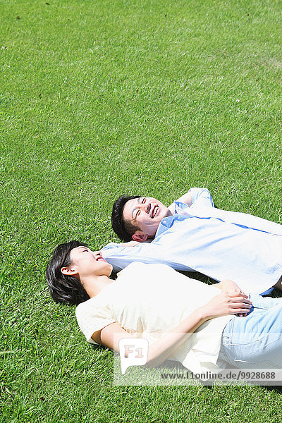 Happy Japanese couple laying on grass in a park