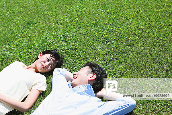 Happy Japanese couple laying on grass in a park