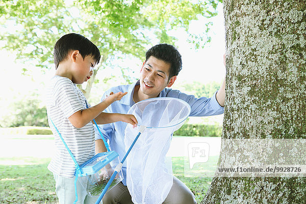 Happy Japanese father and son catching insects in a city park