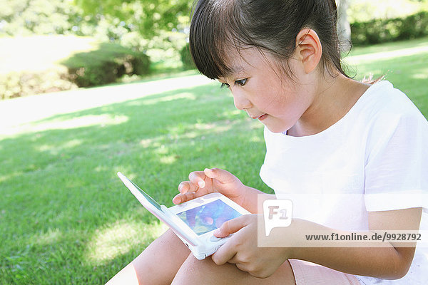 Japanese young girl playing video games in a city park