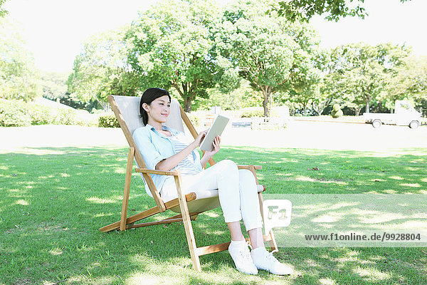 Japanese woman with tablet on deck chair in a city park