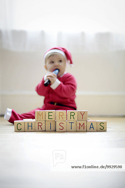 Ein kleiner Junge  der als Weihnachtsmann verkleidet ist  mit Spielzeugblöcken  in denen er Frohe Weihnachten liest.