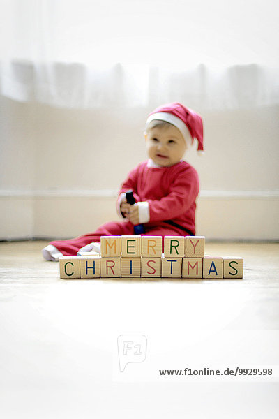 Ein kleiner Junge  der als Weihnachtsmann verkleidet ist  mit Spielzeugblöcken  in denen er Frohe Weihnachten liest.