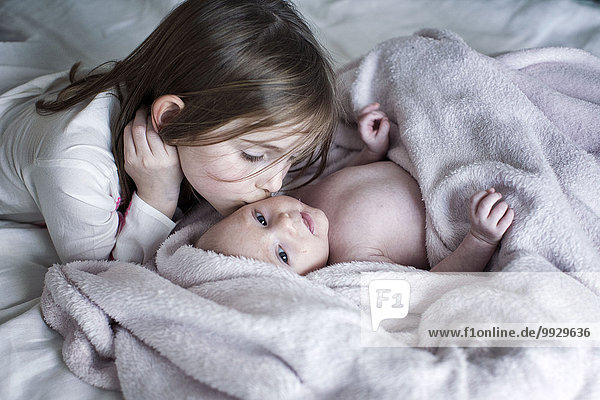 Little girl kissing baby brother's cheek on bed