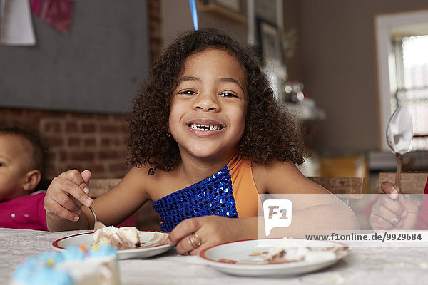 Mixed race girl eating cake at table