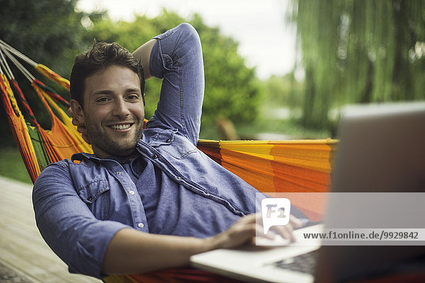 Man reclining in hammock using laptop computer