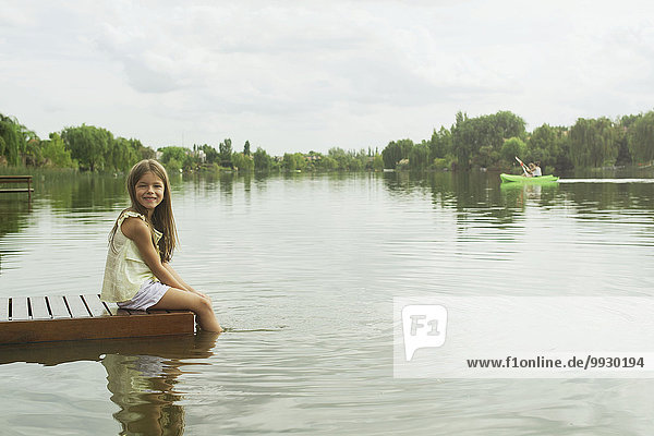 Girl sitting on dock with feet dangling in lake  portrait