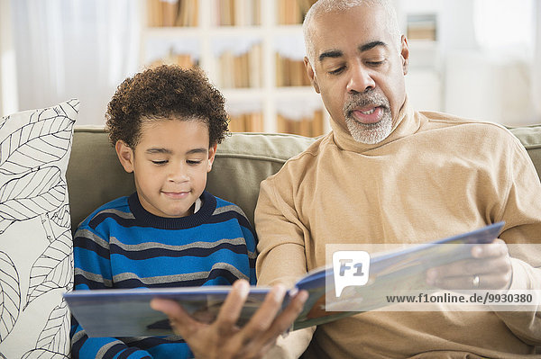 Mixed race grandfather and grandson reading book on sofa