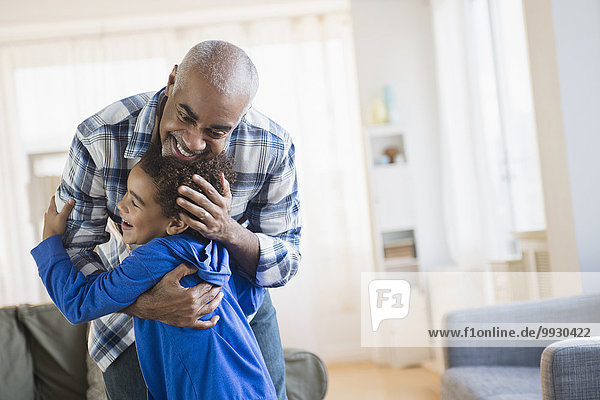 Mixed race grandfather and grandson hugging in living room