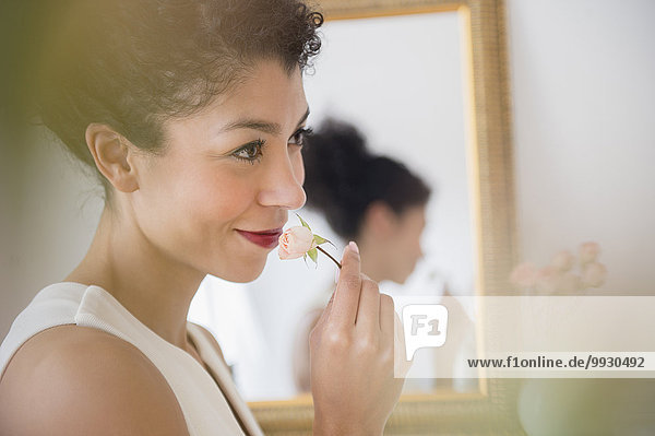Mixed race woman smelling flower near mirror