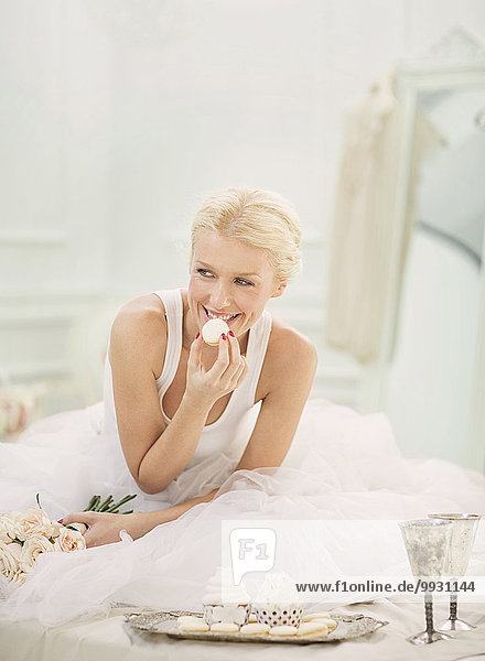 Smiling bride eating cupcakes on bed