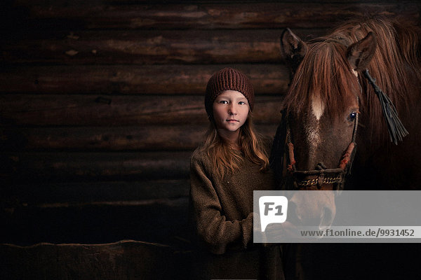 Caucasian girl standing with horse in barn